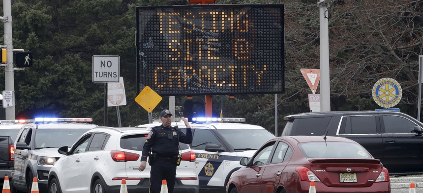A police officer waves traffic past the entrance to a drive-through COVID-19 testing center after it reached capacity in Paramus, N.J., Friday, March 20, 2020.