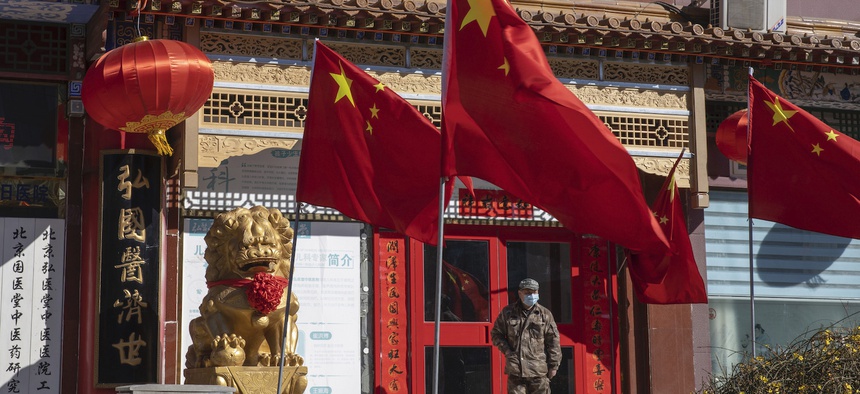 In this photo taken Tuesday, March 3, 2020, a worker stands near Chinese national flag and propaganda which reads "Go China" in Beijing.