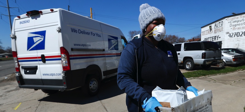 A United States Postal worker makes a delivery with gloves and a mask in Warren, Mich., Thursday, April 2, 2020.