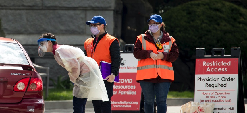 Workers direct people as Children's National Hospital tests children and young adults for COVID-19 at a drive-through (drive-in) testing site at Trinity University, Thursday, April 16, 2020, in Washington.