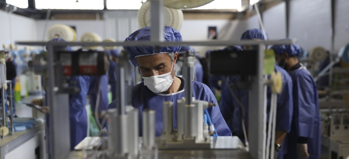 A worker wearing a protective suit operates a machine which makes face masks at a factory in Eshtehard, some 70 miles (114 kilometers) west of the capital Tehran, Iran, Tuesday, April 14, 2020.