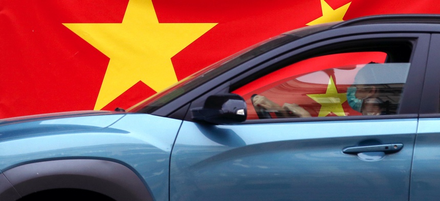 In this April 13, 2020, photo, a woman wearing a face mask drives her car by a Chinese flag placed on a street prior a curfew set up to help prevent the spread of the new coronavirus in Belgrade, Serbia.