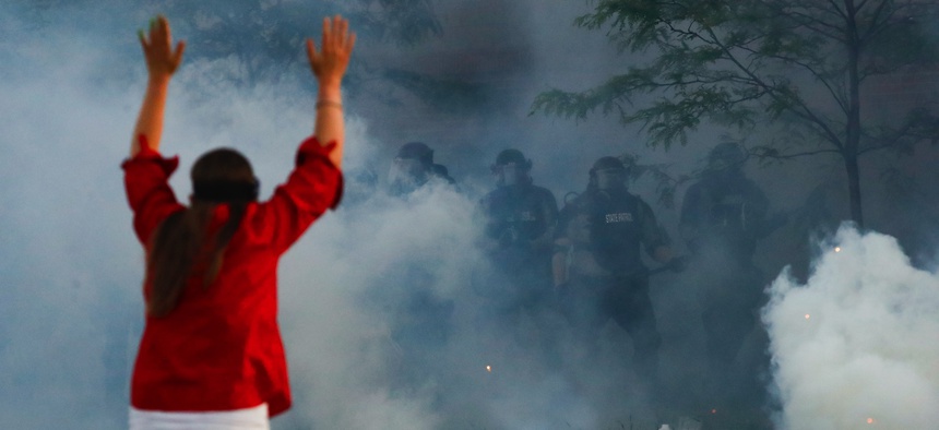 Tear gas canisters detonate beside a protester as authorities clear an intersection near the Minneapolis 5th Police Precinct, Saturday, May 30, 2020, in Minneapolis.