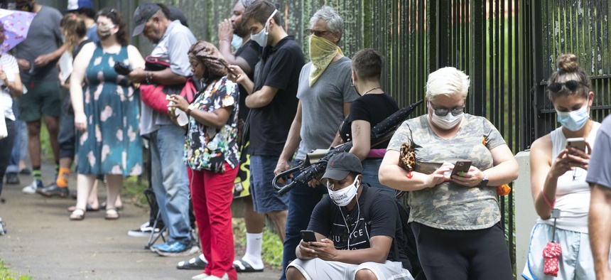 In this June 9, 2020, file photo, Steven Posey checks his phone as he waits in line to vote at Central Park in Atlanta. Voters reported wait times of three hours.