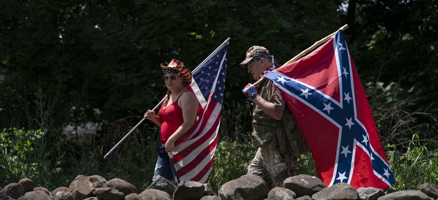 Tourists carry an American flag and a Confederate flag as they walk on a pathway at the Gettysburg National Military Park, Saturday, July 4, 2020, in Gettysburg, Pa.
