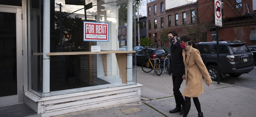 Pedestrians wearing masks pass an empty storefront with a "For Rent" sign in the Red Hook neighborhood of Brooklyn, Tuesday, May 12, 2020, in New York.