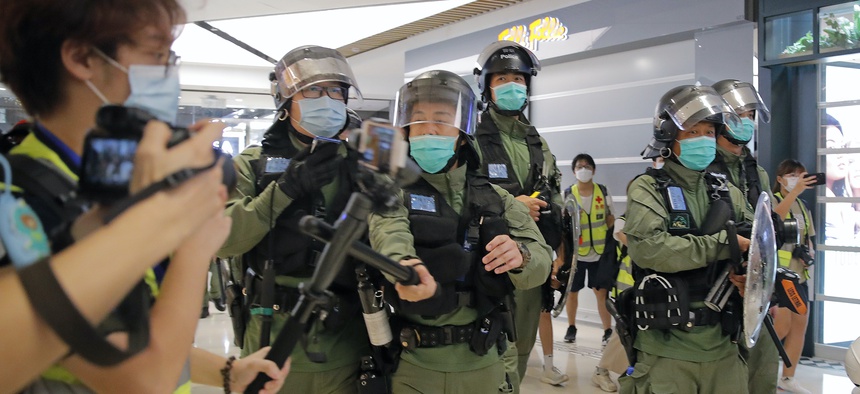 A riot police officer uses baton to hit a journalist's microphone during a protest to mark one-year anniversary of the Yuen Long subway attack, at a shopping mall in Hong Kong, Tuesday, July 21, 2020.