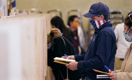 Bruce Lowell looks down at his ballot as he enters a voting booth at an early voting location, Tuesday, Oct. 27, 2020, in Lowell, Mass.