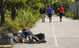 A homeless person lies down along the Hudson River Park walkway in New York City as people pass her by.