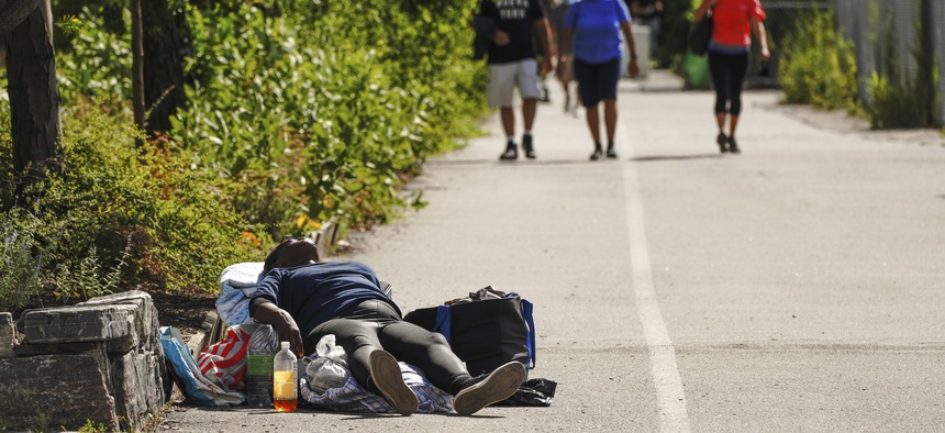 A homeless person lies down along the Hudson River Park walkway in New York City as people pass her by.