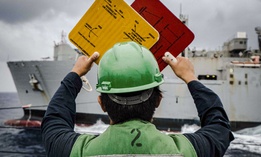 A U.S. Navy sailor signals from the guided-missile destroyer USS John S. McCain to the supply ship USNS Alan Shepard during a replenishment in the South China Sea, Oct. 22, 2020.