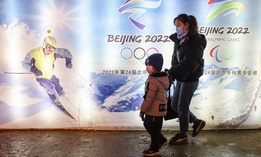 People wear protective masks as they walk front the logos of the 2022 Beijing Winter Olympics at Yanqing Ice Festival on February 26, 2021 in Beijing, China.