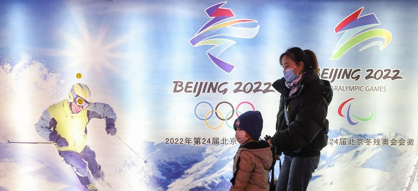 People wear protective masks as they walk front the logos of the 2022 Beijing Winter Olympics at Yanqing Ice Festival on February 26, 2021 in Beijing, China.